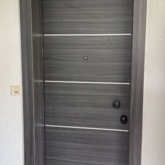 Θωρακισμένη πόρτα σε ανθρακί απόχρωση με ίνοξ και μαύρες λεπτομέρειες, κατασκευασμένη από το επιπλοποιείο μας Wood Design Πάτσης στην Πτολεμαΐδα.