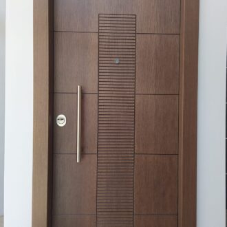 Porta 1 Θωρακισμένη πόρτα σε βαμμένο καφέ δρυς, με σκαλιστό σχέδιο και ίνοξ λεπτομέρειες, κατασκευασμένη από το επιπλοποιείο μας Wood Design Πάτσης στην Πτολεμαΐδα.